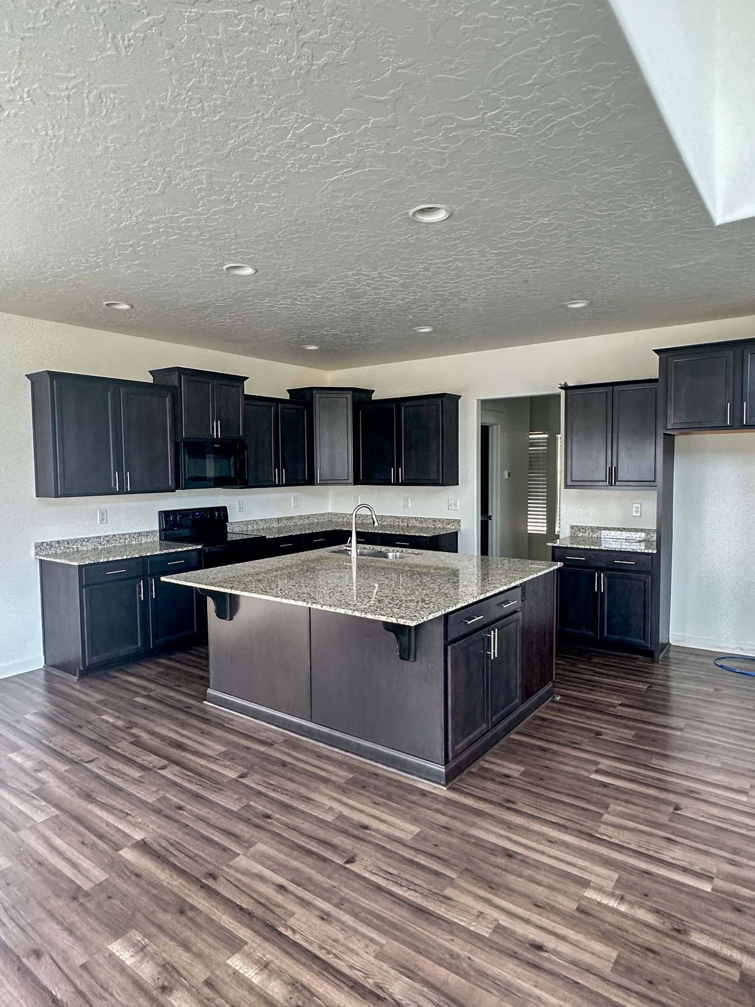 Kitchen featuring light stone counters, a center island with sink, a breakfast bar area, black appliances, and dark wood finished floors