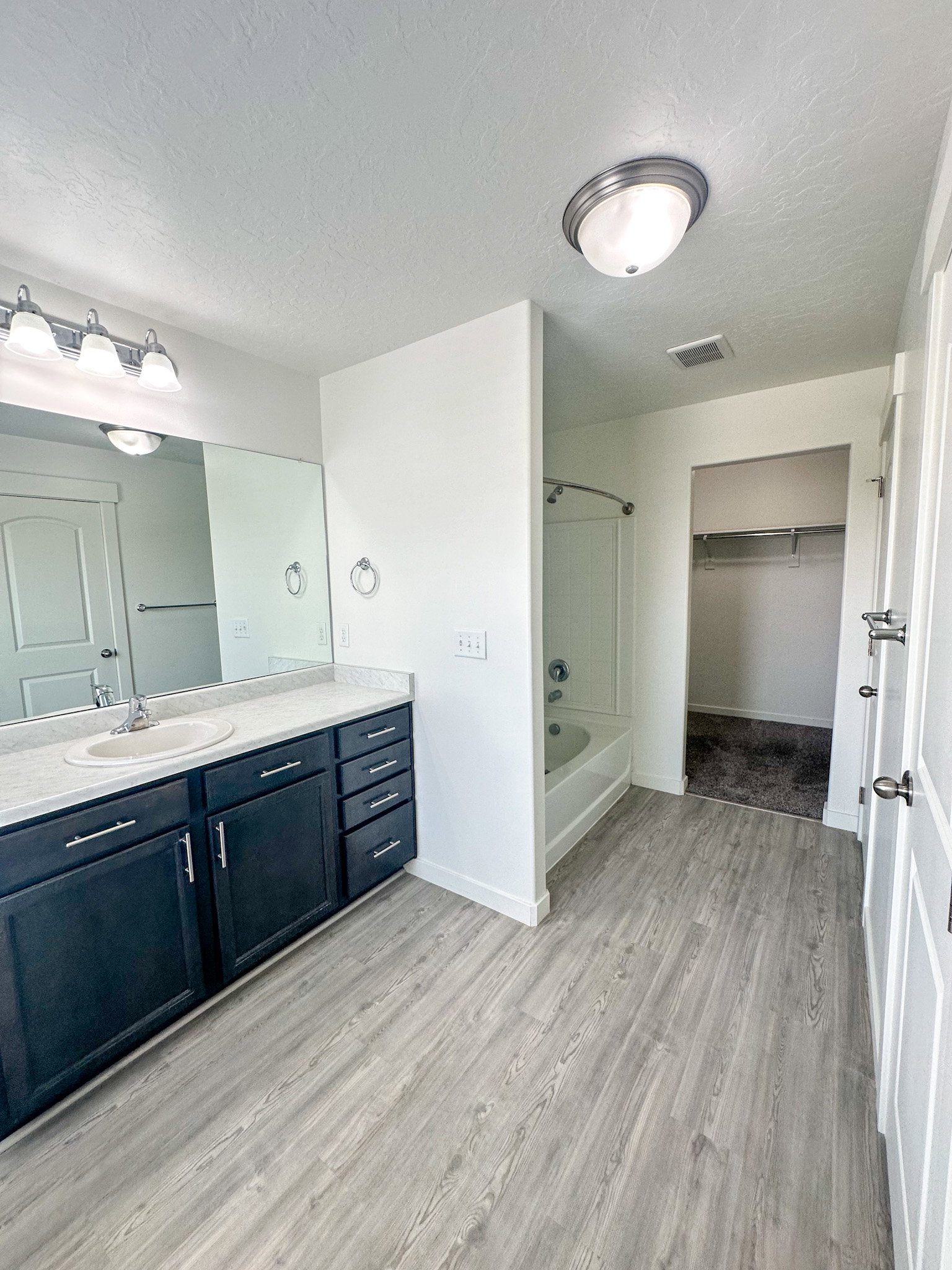 Bathroom with vanity, a textured ceiling, light wood-style flooring, a walk in closet, and shower / tub combination