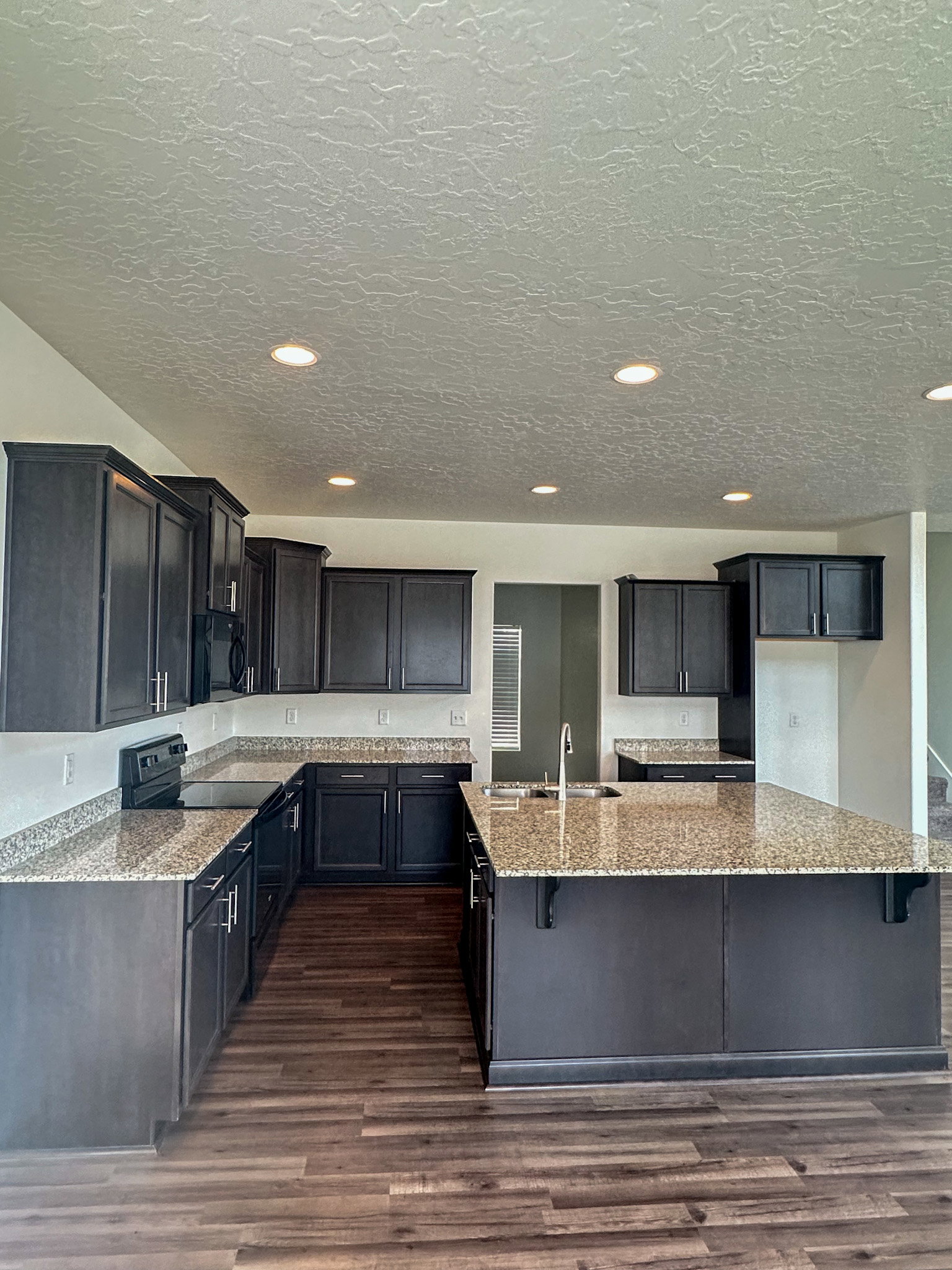 Kitchen with a kitchen breakfast bar, light stone countertops, black appliances, an island with sink, and dark wood-type flooring