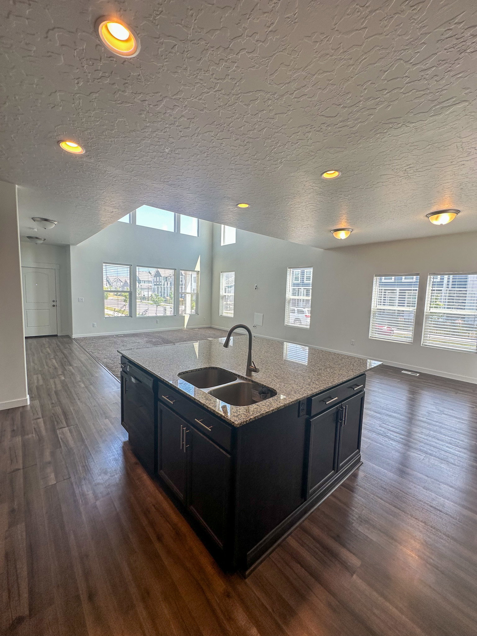 Kitchen featuring open floor plan, dark cabinets, light stone countertops, an island with sink, and dark wood-type flooring