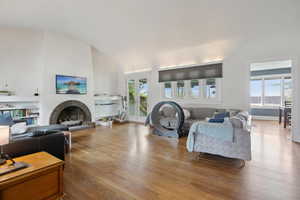Living room with a barrel ceiling, wood finished floors, a brick fireplace, built in features, and french doors