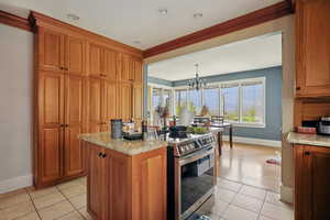 Kitchen featuring stainless steel electric stove, wood finish cabinetry, suspended lighting, a center island, and light tile patterned floors