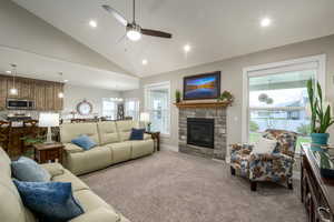 Carpeted living area featuring a ceiling fan, lofted ceiling, suspended lighting, and a stone fireplace
