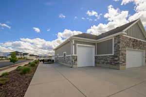 View of property exterior with stone siding, board and batten siding, a garage, and concrete driveway