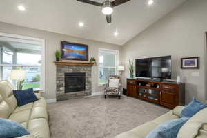 Living room featuring light colored carpet, recessed lighting, a stone fireplace, vaulted ceiling, and ceiling fan
