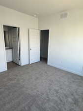 Unfurnished bedroom featuring dark colored carpet and ensuite bathroom