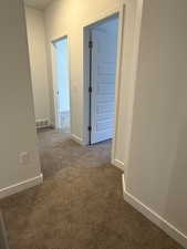 Hallway featuring baseboards and dark colored carpet