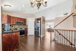 Kitchen with stainless steel appliances, dark wood-style floors, vaulted ceiling, suspended lighting, and tasteful backsplash