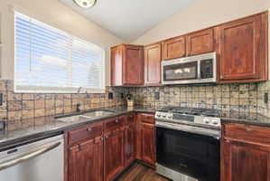 Kitchen with stainless steel appliances, vaulted ceiling, dark stone countertops, dark wood-style floors, and backsplash