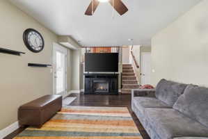 Living area featuring ceiling fan, dark wood-style floors, and a warm lit fireplace