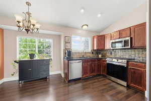 Kitchen with stainless steel appliances, lofted ceiling, hanging lights, dark wood-style floors, and backsplash