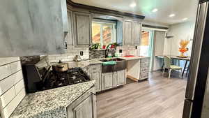 Kitchen with light stone countertops, stainless steel fridge, light wood finished floors, black gas range, and tasteful backsplash