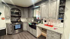 Kitchen featuring stainless steel appliances, light stone countertops, backsplash, and dark wood finished floors