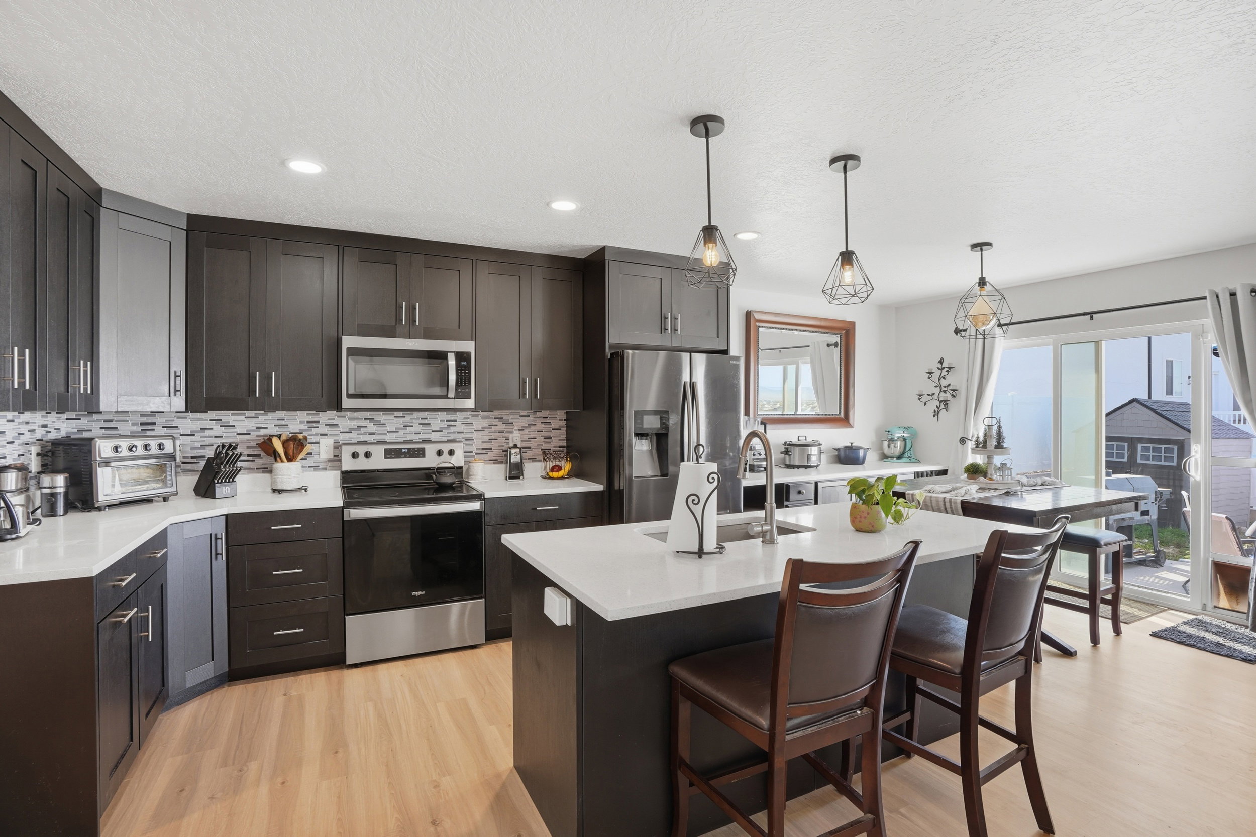 Kitchen with stainless steel appliances, light wood-type flooring, a kitchen breakfast bar, decorative light fixtures, and an island with sink