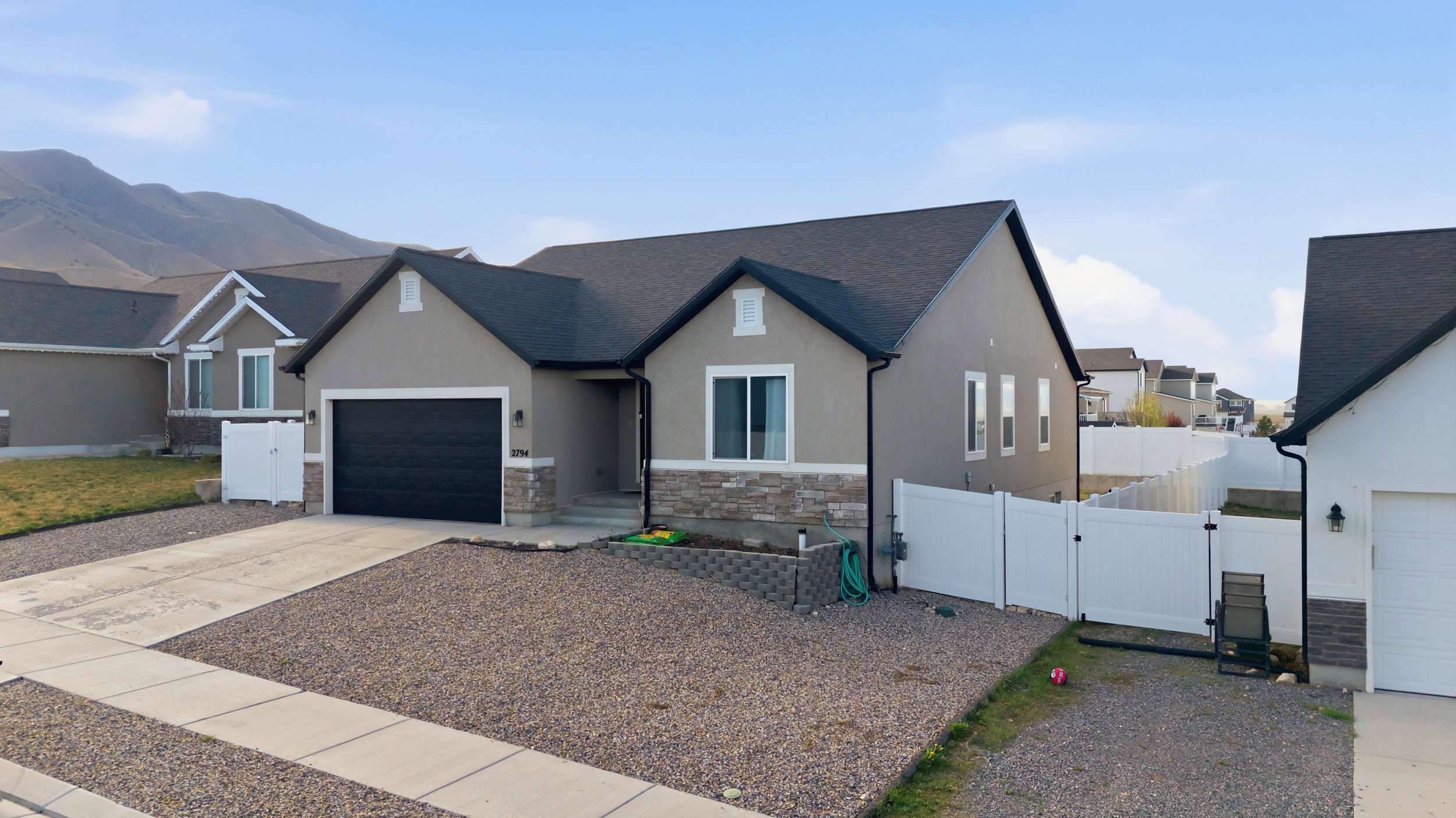 View of front of property featuring a gate, stone siding, driveway, stucco siding, and a garage