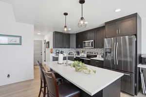 Kitchen with stainless steel appliances, a kitchen breakfast bar, an island with sink, light wood-style floors, and pendant lighting