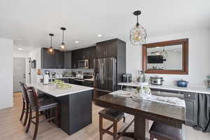 Kitchen featuring stainless steel appliances, a kitchen bar, light wood-style floors, a kitchen island with sink, and pendant lighting