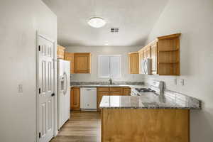 Kitchen with open shelves, white appliances, a peninsula, a textured wall, and light wood-style floors