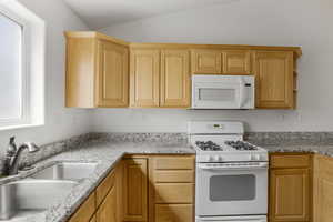Kitchen featuring white appliances, light stone countertops, light wood finish cabinetry, and vaulted ceiling