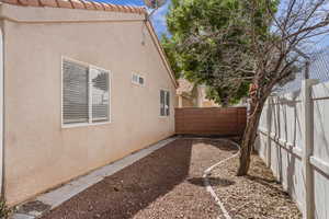 View of side of property with a fenced backyard, stucco siding, and a tiled roof