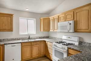 Kitchen with white appliances, light stone countertops, vaulted ceiling, light wood finished floors, and light wood finish cabinets