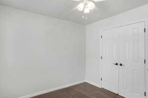 Unfurnished bedroom featuring dark colored carpet, a ceiling fan, and a closet