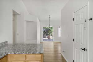 Kitchen with light stone counters, hanging lights, light wood-style floors, and a peninsula