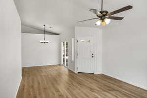 Entryway featuring light wood-style flooring, a ceiling fan, a chandelier, and vaulted ceiling
