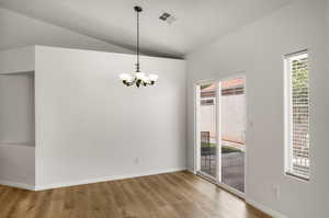 Unfurnished dining area with suspended lighting, vaulted ceiling, and light wood-style flooring