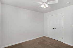 Unfurnished bedroom featuring dark colored carpet, a ceiling fan, and a closet