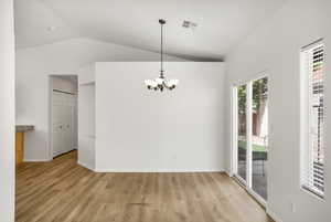 Unfurnished dining area with vaulted ceiling, hanging lights, and light wood finished floors