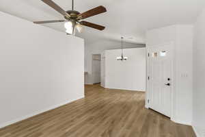 Unfurnished living room featuring vaulted ceiling, light wood-style flooring, a chandelier, and a ceiling fan