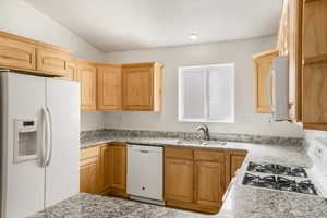 Kitchen featuring white appliances, vaulted ceiling, light wood finish cabinets, and light stone counters