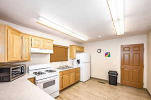 Kitchen featuring light countertops, white appliances, light wood finished floors, light wood finish cabinetry, and a textured ceiling
