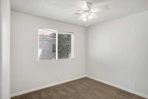 Empty room featuring a ceiling fan and dark colored carpet