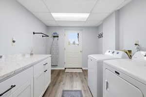 Laundry area with light wood-style flooring, a drop ceiling, separate washer and dryer, and cabinet space