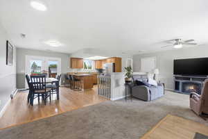 Living room with light wood-type flooring, a fireplace with flush hearth, a baseboard heating unit, and ceiling fan