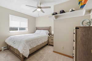 Bedroom with baseboard heating, light carpet, and a ceiling fan