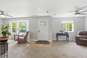 Foyer entrance with ceiling fan, light colored carpet, and a baseboard radiator