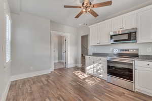 Kitchen with stainless steel appliances, white cabinets, ceiling fan, and dark wood-style flooring
