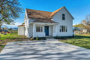View of front of property with covered porch, a shingled roof, and a front yard