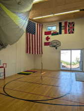 Indoor activity space featuring polished wood flooring with court lines, concrete block walls, and a wood-paneled ceiling