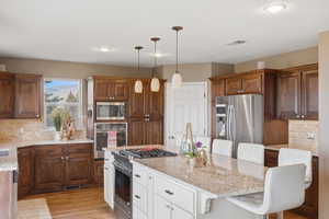 Kitchen with decorative backsplash, a breakfast bar, light stone countertops, dual tone cabinetry, and stainless steel appliances