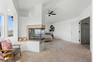 Sitting room with a multi sided fireplace, ceiling fan, carpet flooring, lofted ceiling, and healthy amount of natural light