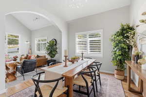 Dining area featuring lofted ceiling, light wood finished floors, healthy amount of natural light, arched walkways, and suspended lighting