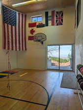 Recreational room featuring wood-finish flooring with court markings, a wall-mounted basketball hoop, high ceilings, and sliding glass doors providing outdoor access