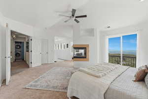 Carpeted bedroom featuring stacked washer / drying machine, access to outside, ceiling fan, vaulted ceiling, and a multi sided fireplace