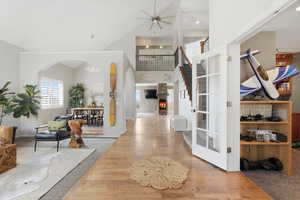 Entryway featuring light wood-type flooring, a warm lit fireplace, a high ceiling, a chandelier, and ceiling fan