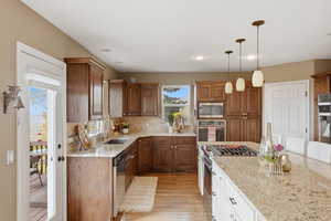 Kitchen featuring light stone countertops, two tone cabinetry, stainless steel appliances, light wood finished floors, and backsplash