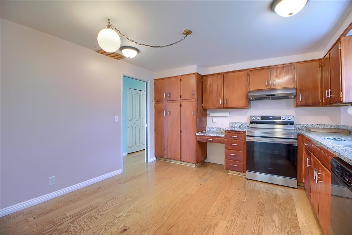 Kitchen featuring electric range, wood finish cabinetry, dishwasher, light wood-style flooring, and light stone counters
